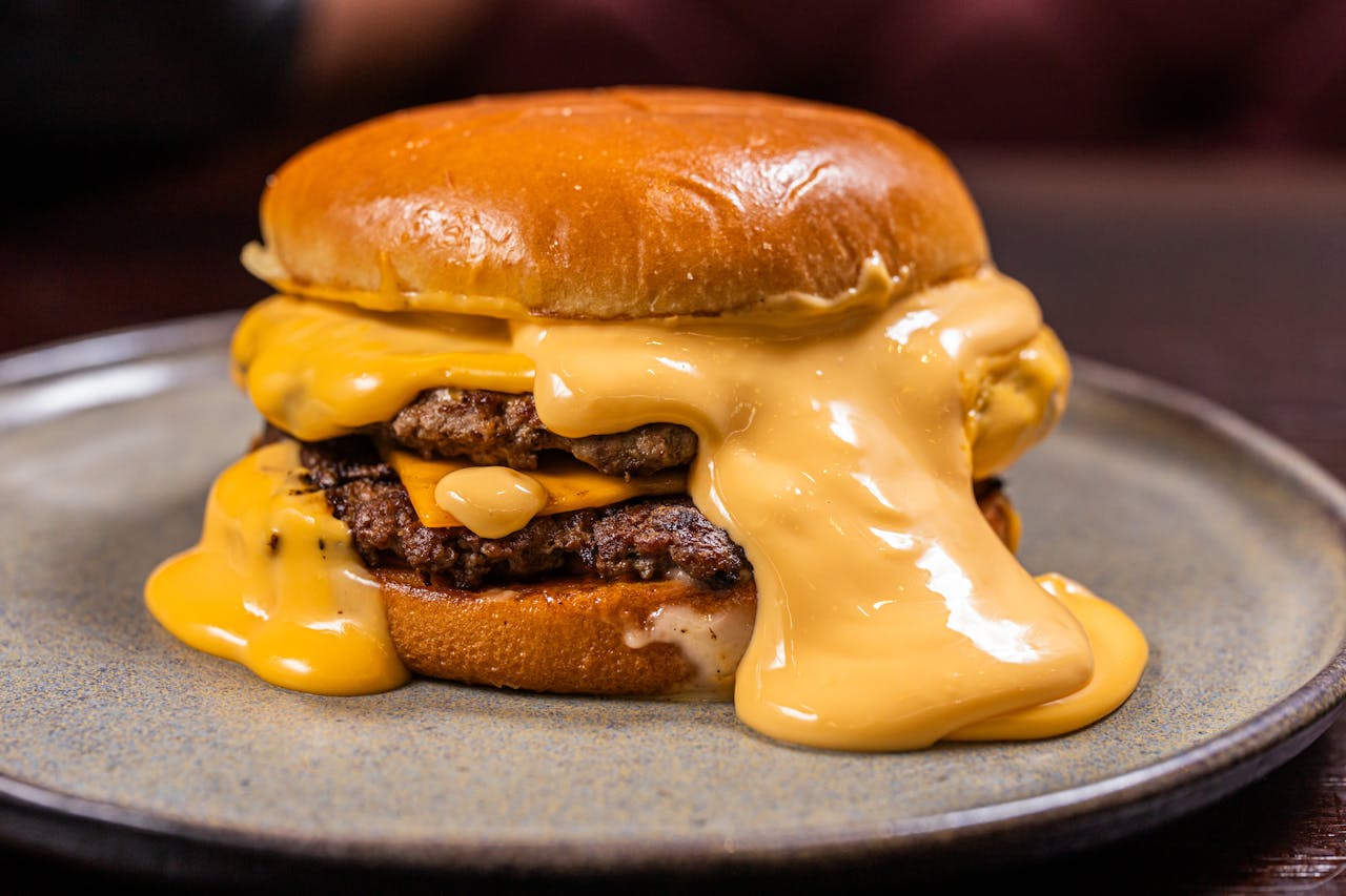 Close-up of a juicy burger with thick melted cheddar cheese, served on a plate.